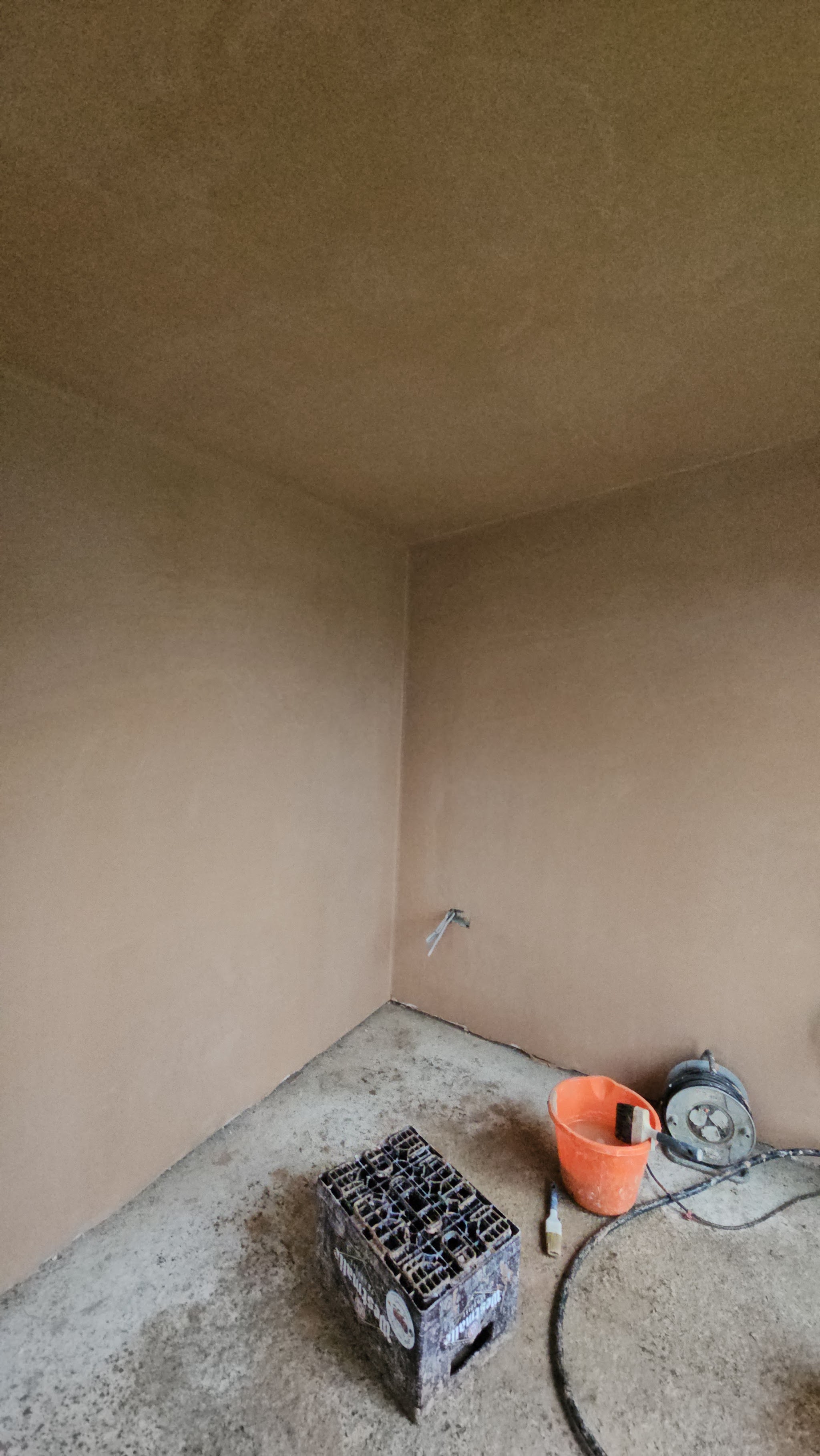 A newly skimmed room, still drying, with the mixing tub and tools on the floor